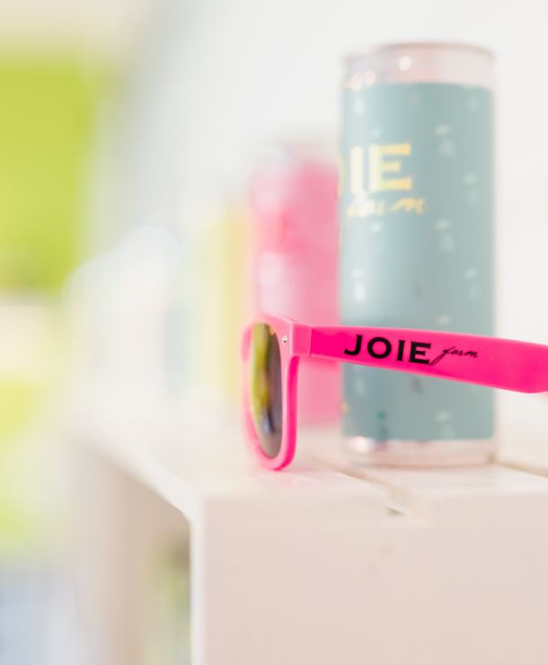 JoieFarm pink sunglasses on shelf with JoieFarm canned beverages